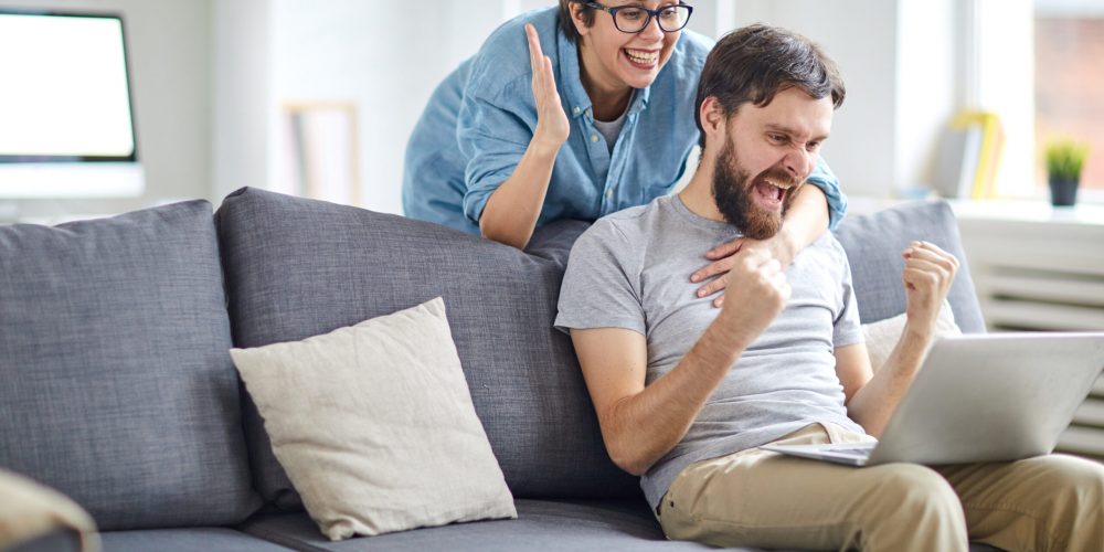 Glad and ecstatic couple expressing triumph while looking at names of winners in lottery on laptop display